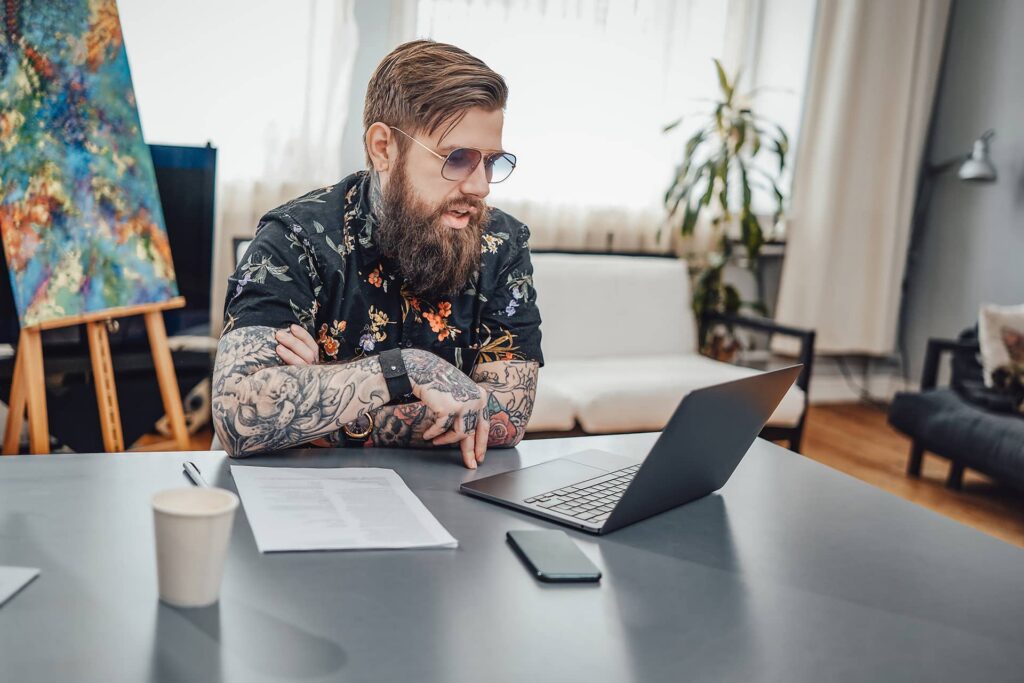 freelancer with beard and sunglasses at home with laptop